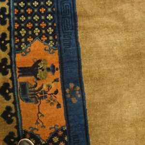 Tan pile rug featuring complex navy and orange borders next to distressed yellow plank flooring.