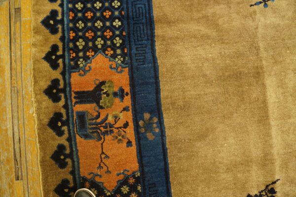 Tan pile rug featuring complex navy and orange borders next to distressed yellow plank flooring.