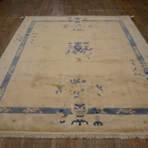 Cream rug with wide blue floral border and vase motifs displayed on wide plank wooden flooring.