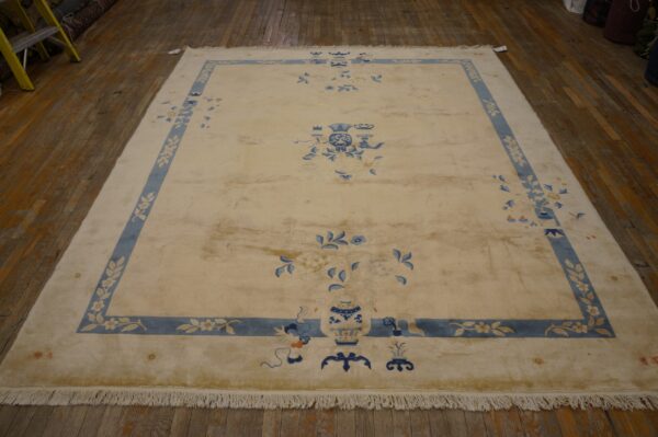 Cream rug with wide blue floral border and vase motifs displayed on wide plank wooden flooring.