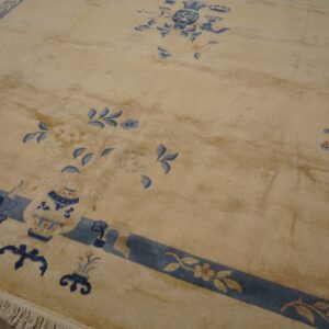 Beige high-pile rug featuring blue floral and vase motifs, framed by a blue border and visible fringe.