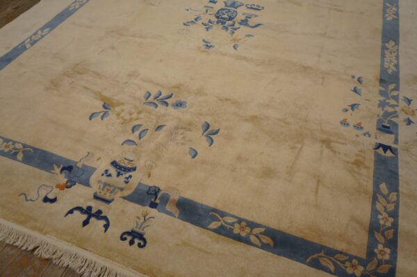 Beige high-pile rug featuring blue floral and vase motifs, framed by a blue border and visible fringe.