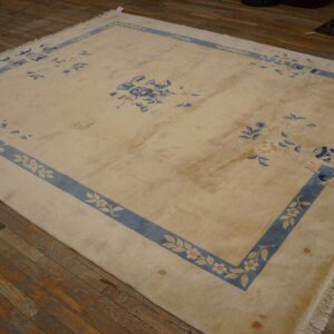A large cream rug with a blue floral border and motifs rests on worn wood flooring.