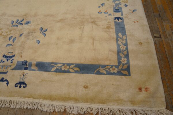 Tan high-pile rug with blue border and blue floral and vase motifs rests on distressed wood flooring.
