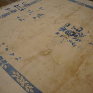 A light beige rug featuring blue decorative motifs and borders rests on dark wooden flooring.