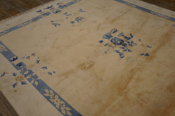 A light beige rug featuring blue decorative motifs and borders rests on dark wooden flooring.