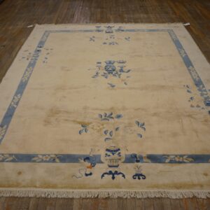 A large cream and blue rug featuring floral vases and a patterned border rests on dark wood flooring.