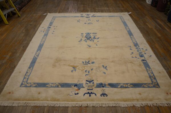 A large cream and blue rug featuring floral vases and a patterned border rests on dark wood flooring.
