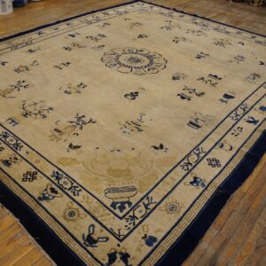 Tan rug with navy blue scattered motifs and borders displayed on distressed hardwood flooring.