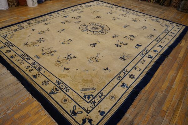Tan rug with navy blue scattered motifs and borders displayed on distressed hardwood flooring.