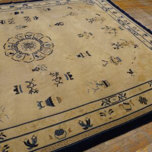 Tan rug with navy borders and blue scattered vase and floral motifs on rustic wood planks.