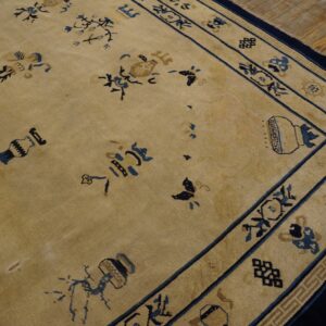 Beige low-pile rug with scattered blue floral and vase motifs and an ornate border resting on wood planks.
