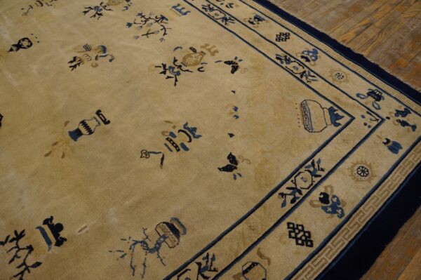 Beige low-pile rug with scattered blue floral and vase motifs and an ornate border resting on wood planks.