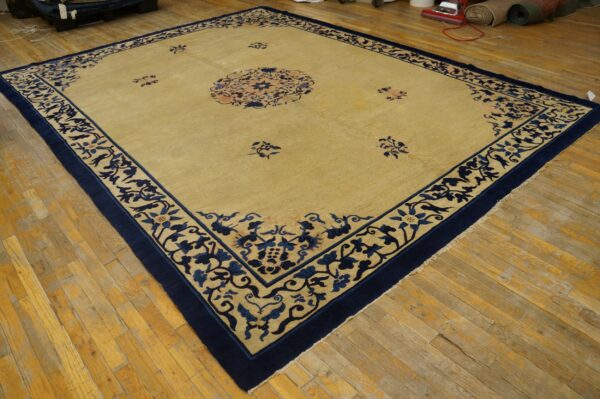 Gold and navy blue floral rug with a central design resting on light, worn plank flooring.