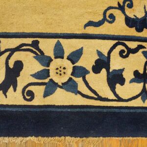 Detailed view of a tan and navy blue rug border with floral pattern and fringe on wood floor.