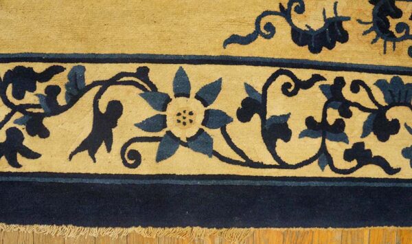 Detailed view of a tan and navy blue rug border with floral pattern and fringe on wood floor.