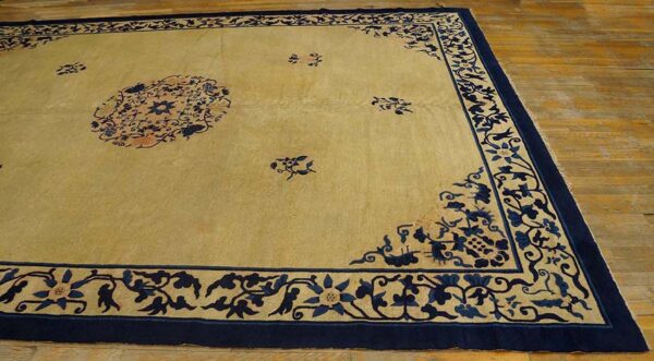 Light beige area rug with a navy blue floral medallion, scatter motifs, and wide border on wood floor.