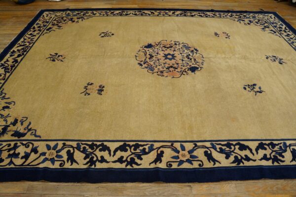 Large tan rug with dark blue floral patterns and a central medallion on hardwood floors.