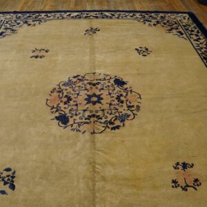 A light tan rug with a navy floral border and center medallion lies on exposed hardwood floors.