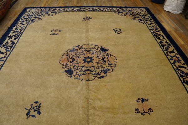 A light tan rug with a navy floral border and center medallion lies on exposed hardwood floors.