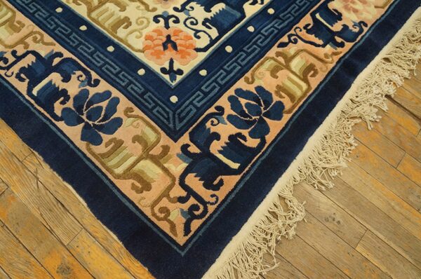 Beige, navy, and orange patterned rug corner featuring fringes resting on distressed wood flooring.