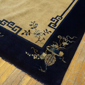 Low-pile beige and navy rug with detailed floral and geometric borders on rustic hardwood planks.