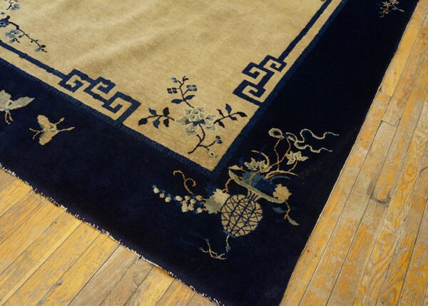 Low-pile beige and navy rug with detailed floral and geometric borders on rustic hardwood planks.