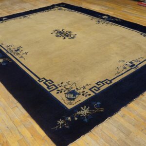 Large tan rug with a wide navy blue border featuring geometric key and delicate floral patterns on wood planks.