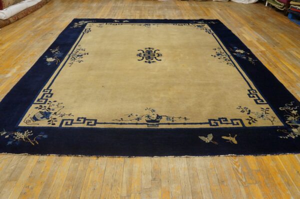 Large beige rug with a wide navy blue border features floral motifs and a central blue medallion on wood flooring.