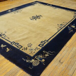 Rectangular tan rug with a wide navy blue border featuring floral and key patterns on a wood floor.