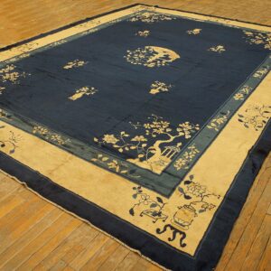Large low-pile blue rug with a tan border and Chinoiserie patterns sits on distressed wood flooring.
