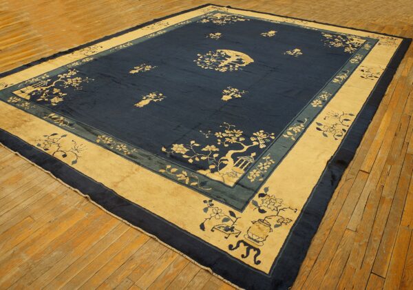 Large low-pile blue rug with a tan border and chinoiserie patterns sits on distressed wood flooring.