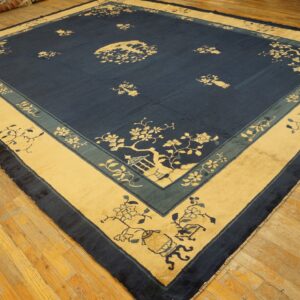 A large square rug with a navy blue field and beige/teal borders, featuring floral motifs on a worn wood floor.
