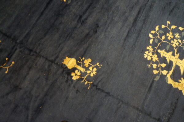 Dark navy rug surface with stylized gold and gray-green floral and botanical patterns.