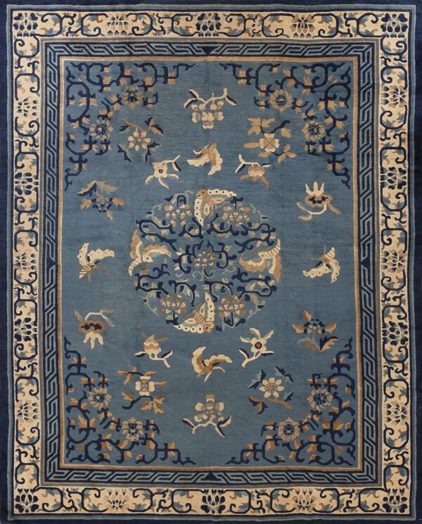 Dusty blue rug with stylized tan and navy floral patterns, framed by complex fretwork and vine borders.