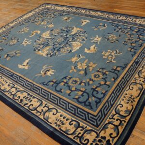 Blue and beige square rug with stylized bird and floral patterns rests on wide plank wood floors.