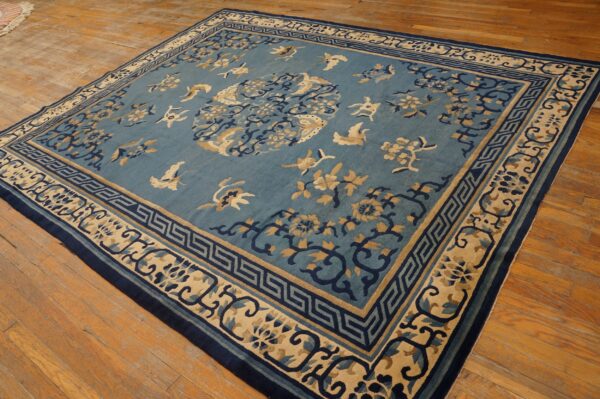 Blue and beige square rug with stylized bird and floral patterns rests on wide plank wood floors.