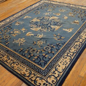 Blue rug with tan and navy floral and bird motifs, featuring a detailed geometric border on wood floors.