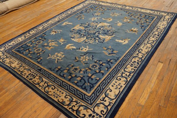 Blue rug with tan and navy floral and bird motifs, featuring a detailed geometric border on wood floors.