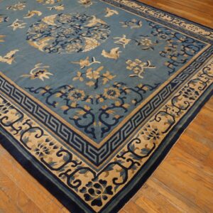 Muted blue rug with dark blue and tan bird and floral motifs lies on distressed wood flooring.