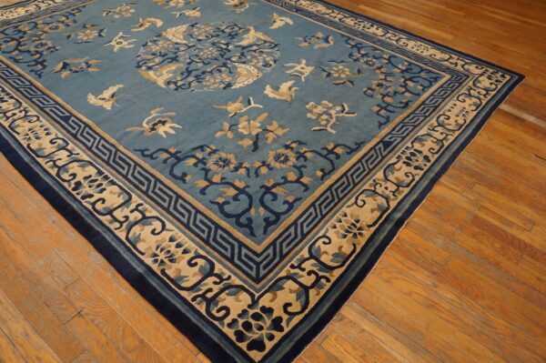 Muted blue rug with dark blue and tan bird and floral motifs lies on distressed wood flooring.