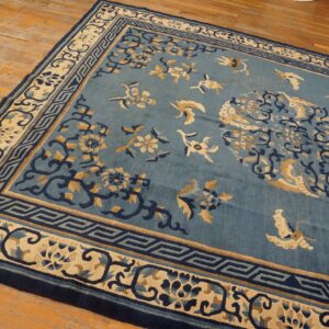 Blue rug with intricate cream and dark blue floral patterns rests on worn light brown hardwood floors.