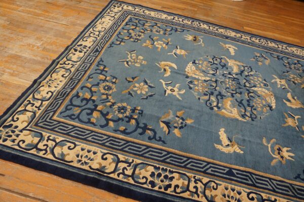 Blue rug with intricate cream and dark blue floral patterns rests on worn light brown hardwood floors.