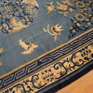 A blue rug featuring tan and navy floral motifs and key borders lies on light wood flooring.