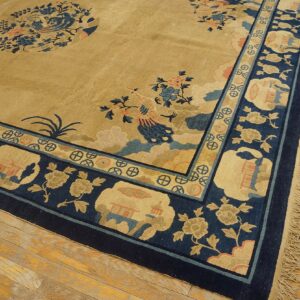 Tan and navy low-pile rug with elaborate bird and floral motifs rests on worn wooden flooring.