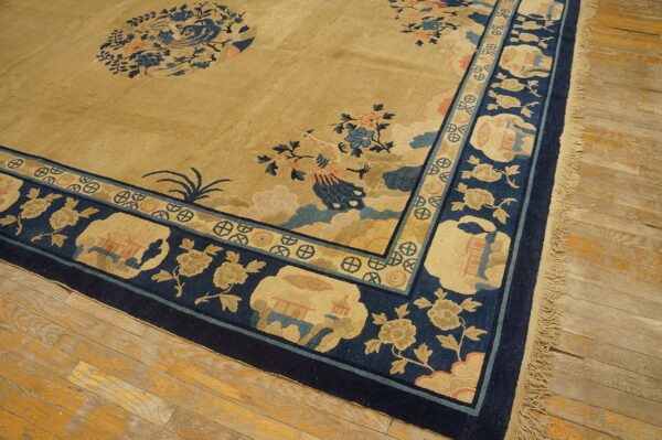 Tan and navy low-pile rug with elaborate bird and floral motifs rests on worn wooden flooring.