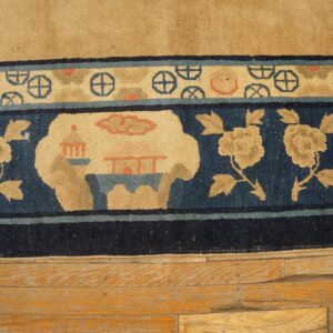 Tan rug with dark blue borders featuring flowers, structures, and wheel motifs on distressed wood plank flooring.