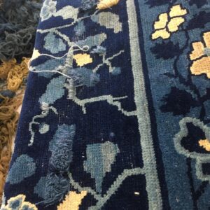Detailed view of a navy blue floral rug with light blue and beige elements and visible loose repair knots.