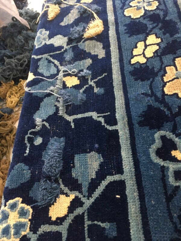 Detailed view of a navy blue floral rug with light blue and beige elements and visible loose repair knots.