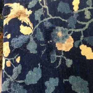 Close-up of a navy rug featuring light blue and cream floral patterns with damaged and frayed areas.